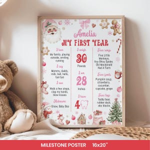 May include: A framed milestone poster for a baby named Amelia, featuring a pink and white design with Christmas-themed illustrations. The poster includes details about the baby's first year, such as weight, height, favorite foods, and toys. The poster is 16x20 inches.