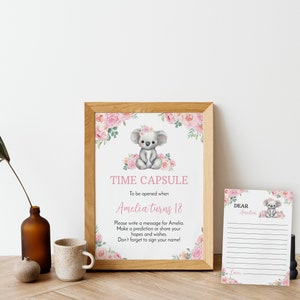 K&ouml;nnte beinhalten: Ein gerahmtes Schild und eine passende Karte mit einer Koala-Illustration und rosa Blumenakzenten. Das Schild tr&auml;gt die Aufschrift TIME CAPSULE To be opened when Amelia turns 18. Please write a message for Amelia. Make a prediction or share your hopes and wishes.