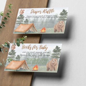 May include: Two cards with a woodland theme. The top card says "Diaper Raffle" and asks guests to bring a pack of diapers for a chance to win a prize. The bottom card says "Books for Baby" and asks guests to bring a book in place of a card. Both cards feature a campfire, a tent, a bear, and a squirrel.