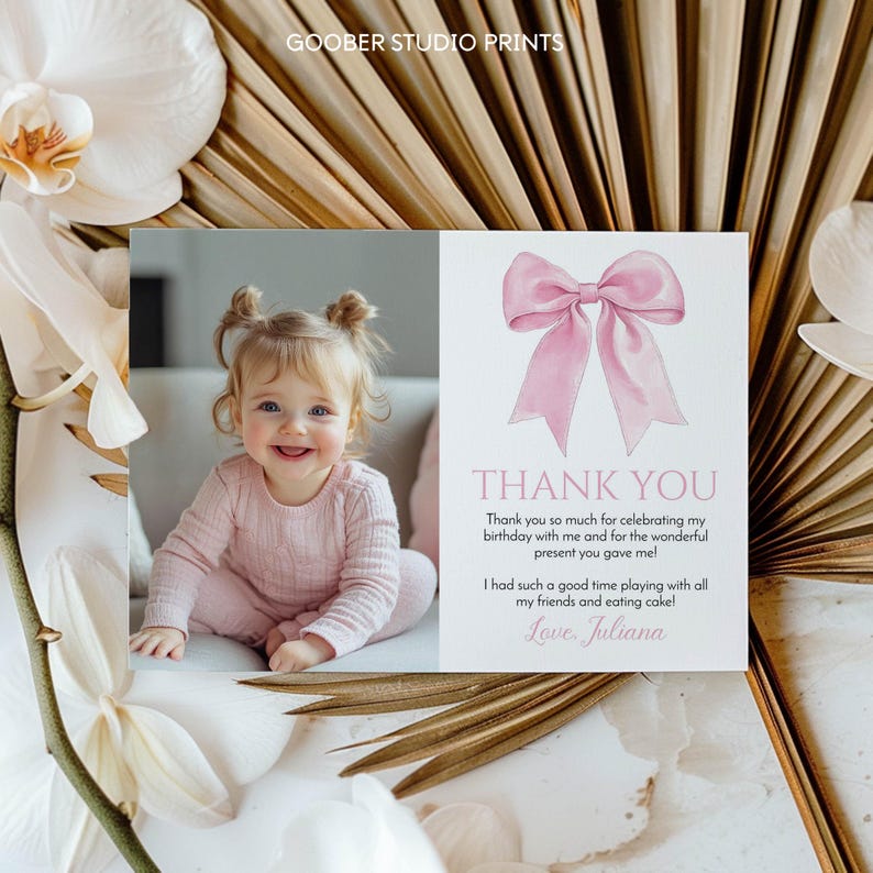 May include: A baby girl in pink clothing smiles in a photograph next to a thank you card. The card features a pink bow illustration and the text "THANK YOU". The card's message expresses gratitude for a birthday celebration and gift.
