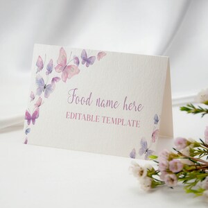Peut inclure: Une carte blanche pli&eacute;e &agrave; la surface textur&eacute;e orn&eacute;e de papillons &agrave; l'aquarelle dans des tons roses et violets. Le texte "Food name here" est imprim&eacute; en police cursive violette, suivi du texte "EDITABLE TEMPLATE" en police rose sans empattement.