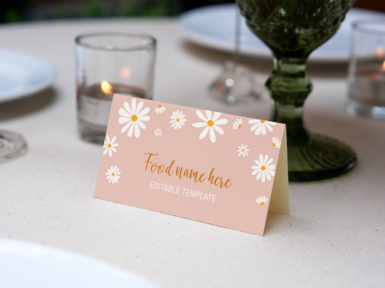 Op de afbeelding: Een gevouwen rechthoekige kaart met een lichtroze achtergrond en een patroon van witte madeliefjes met gele harten. De kaart toont de tekst "Food name here" in een goudkleurig scriptlettertype en "EDITABLE TEMPLATE" in witte hoofdletters.