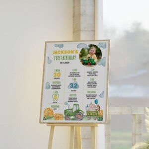 May include: A colorful first birthday poster with a photo of a baby boy in a green tractor. The poster includes details about the baby's age, weight, height, favorite foods, and toys. The poster is decorated with a tractor, hay bales, and clouds.