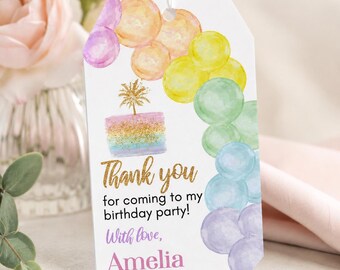 May include: A white rectangular gift tag with a hole at the top, featuring a watercolour rainbow balloon arch, a gold glitter cake illustration, and the text: Thank you for coming to my birthday party! With love, Amelia, in gold and purple script.