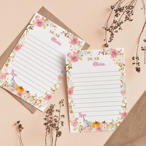 K&ouml;nnte beinhalten: Zwei wei&szlig;e Briefpapierb&ouml;gen mit horizontalen Linien, verziert mit einem Blumenrand aus rosa Rosen, wei&szlig;en Bl&uuml;ten und orangefarbenen K&uuml;rbissen. Der Text "DEAR Olivia," steht oben und "Love," unten auf jedem der beiden Briefpapierb&ouml;gen.