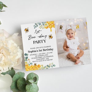 May include: A bee-themed first birthday party invitation with a photo of a baby girl wearing a white dress. The invitation features a yellow honeycomb, bees, and green leaves. The text on the invitation reads "1st Bee-day Party" and "Sophia's 1st Birthday".