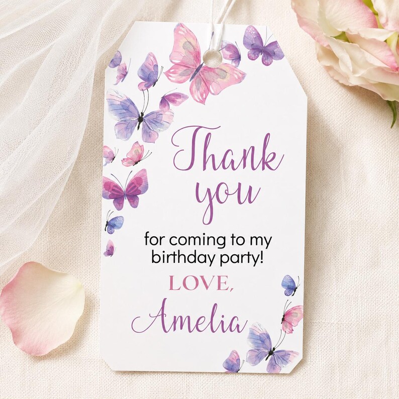 May include: A rectangular white gift tag with a hole at the top, decorated with watercolor-style purple and pink butterflies. The text reads Thank you for coming to my birthday party! LOVE, Amelia in purple and black script and sans-serif fonts.