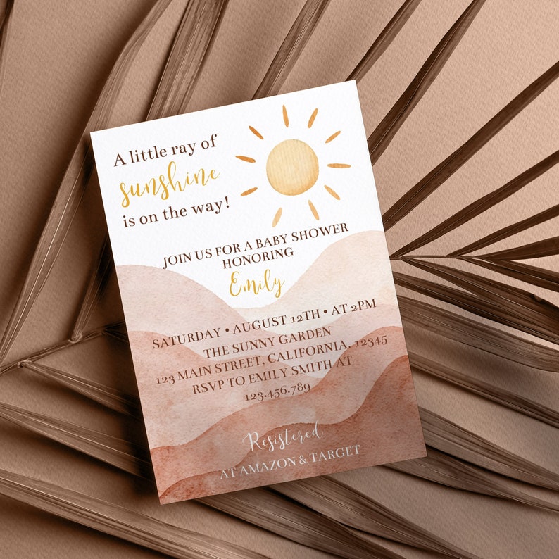 May include: A baby shower invitation with a watercolour background of orange and brown hills. The invitation features a sun with rays and the text "A little ray of sunshine is on the way!"  Join us for a baby shower honouring Emily. Saturday, August 12th at 2pm. The Sunny Garden, 123 Main Street, California, 12345. RSVP to Emily Smith at 123-456-789. Registered at Amazon & Target.