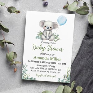 K&ouml;nnte beinhalten: Eine rechteckige, wei&szlig;e Einladungskarte f&uuml;r eine Babyparty mit einer Aquarellillustration eines Koalas, der einen hellblauen Luftballon h&auml;lt, umgeben von gr&uuml;nen Eukalyptusbl&auml;ttern. Der Text lautet: JOIN US FOR A Baby Shower IN HONOR OF Amanda Miller SATURDAY | AUGUST 15TH | AT 2PM AMANDA'S HOUSE 123 MAIN STREET, BOSTON. 1235 RSVP TO ANNA AT 123.456.789 Registered at target.