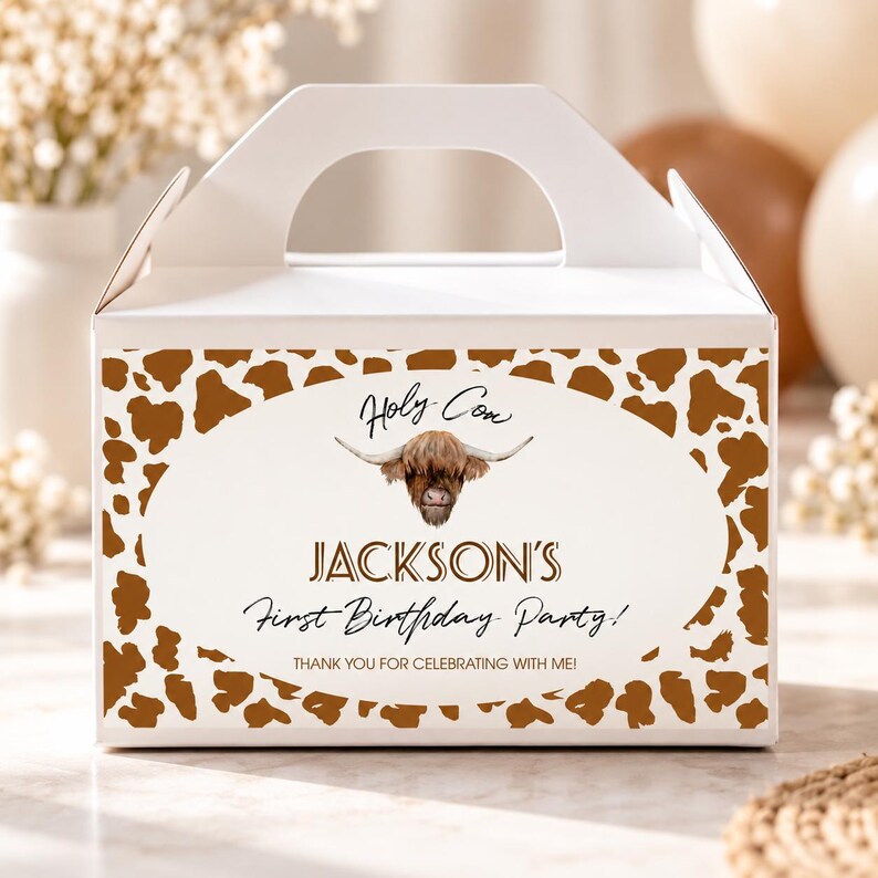 May include: A white cardboard gable box featuring a brown and white cow print border. The center oval graphic displays a Highland cow illustration with the text: Holy Cow, JACKSON'S First Birthday Party! THANK YOU FOR CELEBRATING WITH ME!