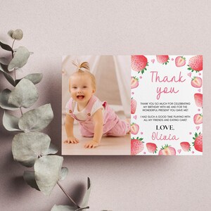 May include: A rectangular thank you card featuring a photograph of a baby on the left and a white background with pink strawberry illustrations and text on the right. The text reads Thank you, thank you so much for celebrating my birthday with me and for the wonderful present you gave me! I had such a good time playing with all my friends and eating cake! Love, Olivia.