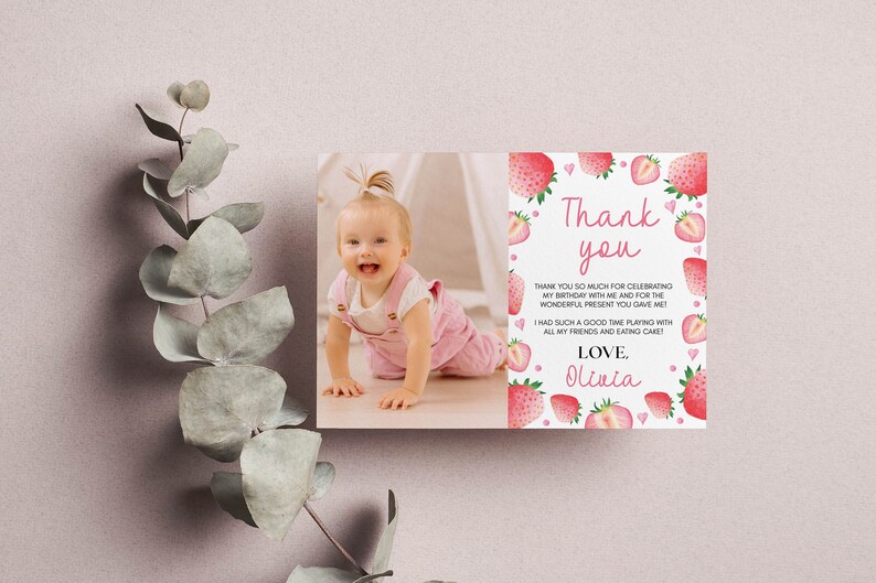 May include: A rectangular thank you card featuring a photograph of a baby on the left and a white background with pink strawberry illustrations and text on the right. The text reads Thank you, thank you so much for celebrating my birthday with me and for the wonderful present you gave me! I had such a good time playing with all my friends and eating cake! Love, Olivia.