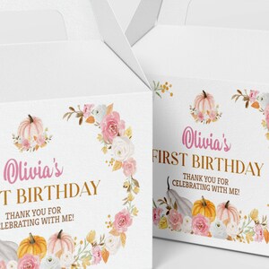 May include: Two white gable boxes featuring a floral wreath design with pink and white roses, orange and pink pumpkins, and gold text that reads Olivia's FIRST BIRTHDAY THANK YOU FOR CELEBRATING WITH ME! The boxes have a handle at the top.