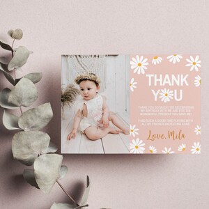 May include: A pink thank you card with white daisies and gold lettering. The card says "Thank You" and "Love, Mila". A photo of a baby girl wearing a white dress and a flower crown is in the background.