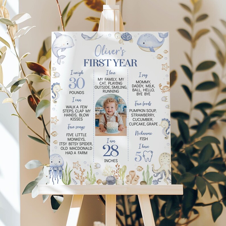 May include: A white milestone board titled Oliver's First Year featuring blue text, a central photo of a child with a cake, and watercolor illustrations of sea creatures including a dolphin, whale, jellyfish, octopus, and seahorses.