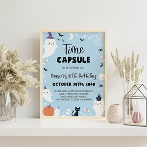 May include: A light blue rectangular sign in a wooden frame featuring Halloween-themed illustrations of ghosts, a black cat, pumpkins, and spiderwebs. The text reads: Time CAPSULE TO BE OPENED ON MASON'S 18th Birthday OCTOBER 30TH, 2040. PLEASE WRITE A MESSAGE.