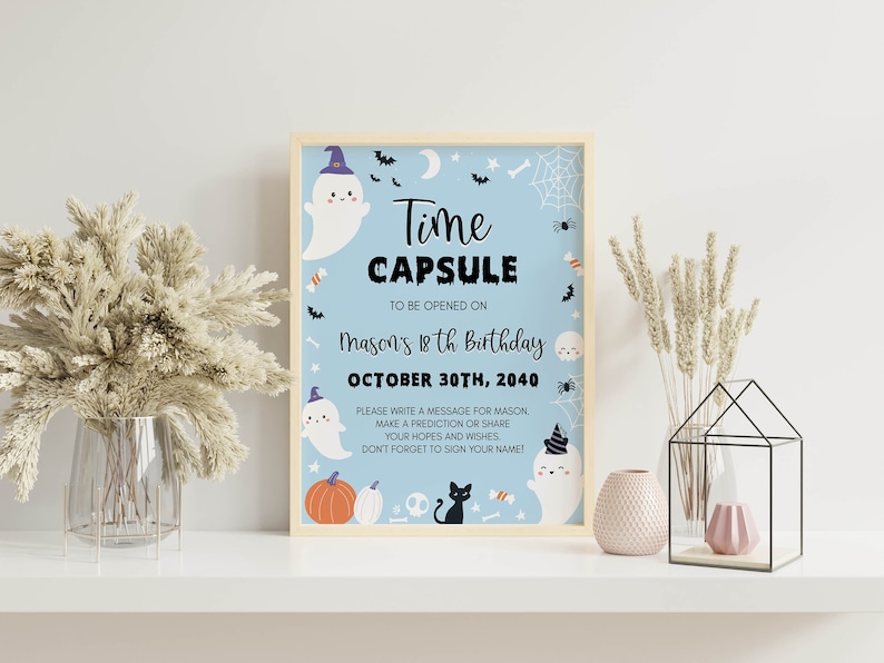 May include: A light blue rectangular sign in a wooden frame featuring Halloween-themed illustrations of ghosts, a black cat, pumpkins, and spiderwebs. The text reads: Time CAPSULE TO BE OPENED ON MASON'S 18th Birthday OCTOBER 30TH, 2040. PLEASE WRITE A MESSAGE.