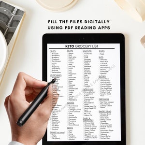 May include: A black and white digital tablet displaying a keto grocery list with checkboxes next to various food items. The list is organized into categories such as fruits, vegetables, meats, seafood, eggs, nuts, fats & oils, dairy & substitutes, flours, dressings, pantry items, and seeds. A hand is holding a black stylus over the tablet.