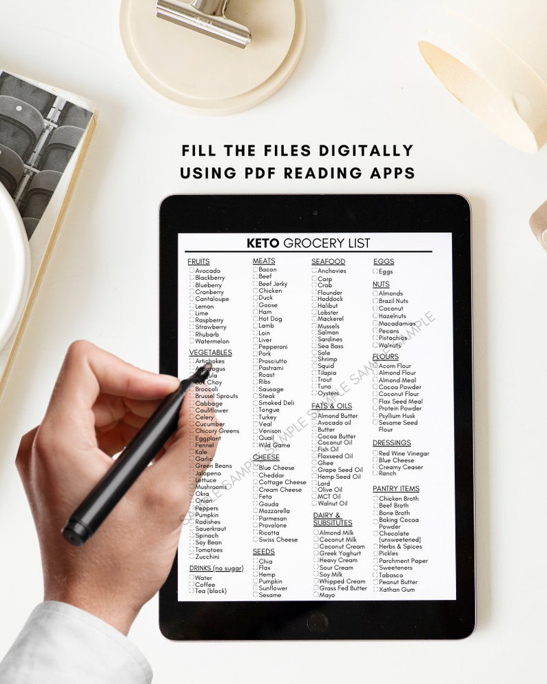 May include: A black and white digital tablet displaying a keto grocery list with checkboxes next to various food items. The list is organized into categories such as fruits, vegetables, meats, seafood, eggs, nuts, fats & oils, dairy & substitutes, flours, dressings, pantry items, and seeds. A hand is holding a black stylus over the tablet.