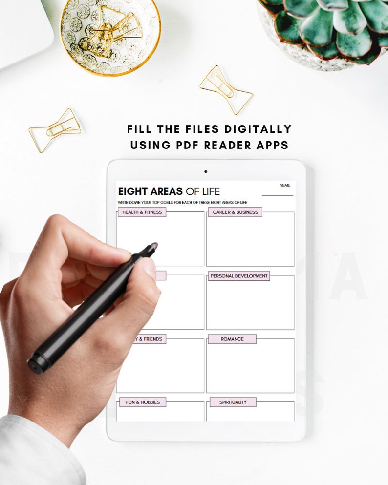 May include: A white tablet with a grid of eight boxes, each labeled with a different area of life: Health & Fitness, Career & Business, Personal Development, Y & Friends, Romance, Fun & Hobbies, Spirituality, and Year. A hand is holding a black marker pen over the tablet.