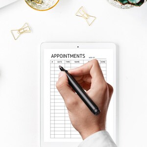 May include: A white tablet with a black grid and the text "APPOINTMENTS" at the top. A hand is holding a black marker and writing on the tablet.