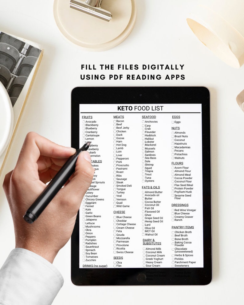 May include: A black tablet with a white screen displaying a keto food list. The list is organized into categories such as fruits, meats, seafood, eggs, nuts, flours, fats & oils, dressings, pantry items, dairy & substitutes, and seeds. The list includes a variety of foods that are commonly consumed on a ketogenic diet.