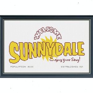 May include: A yellow and red cross-stitch design of a sign that reads "Sunnydale" with a sun and the text "Enjoy your Stay!" below. The sign also includes the text "Population 38,500" and "Established 1903".