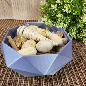 May include: A purple geometric bowl filled with natural elements, including dried sticks, nuts, and a woven straw-like material.