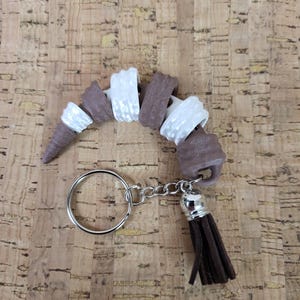 May include: A brown and white spiral keychain with a brown tassel. The keychain is made of a soft, pliable material and has a silver key ring.