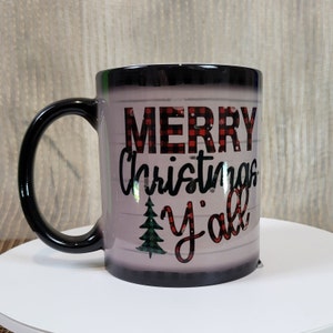 May include: Black and white color changing mug with the text "Merry Christmas y'all" in red and black plaid font. A small green Christmas tree is to the left of the text.
