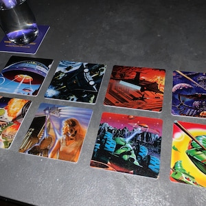 May include: Eight square coasters with colorful illustrations of spaceships, aliens, and futuristic landscapes. The coasters are made of a durable material and are perfect for protecting your furniture from spills and scratches.
