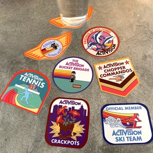 May include: Ten colorful round and rectangular stickers with the Activision logo and various themes, including tennis, flying aces, a bucket brigade, chopper commandos, friends of dolphins, and a ski team.