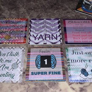 May include: Six colorful square coasters with knitting-themed sayings. The coasters feature different knitting patterns and yarn balls. The sayings include "Knitter? I prefer the term Yarn Goddess", "Behind every great knitter is a huge stash of YARN", "Kitchener stitch Set up: Front purl on Back knit on Repeat: Front knit off Front purl on Back purl off Back knit on", "Don't talk to me I'm Counting", "Feelin' 1 SUPER FINE", and "Just one more row".