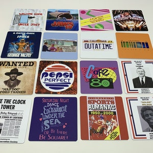 May include: A collection of square coasters with various designs and text. The coasters feature images and text from the movie "Back to the Future", including "OUTATIME" license plate, "Hover Board", and "Cafe 80".