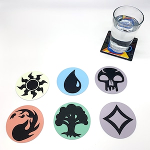 May include: Six round coasters with different Magic: The Gathering symbols. The symbols are a sun, a drop of water, a skull, a diamond, a tree, and a flame. The coasters are on a white surface.