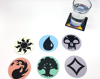 May include: Six round coasters with different Magic: The Gathering symbols. The symbols are a sun, a drop of water, a skull, a diamond, a tree, and a flame. The coasters are on a white surface.