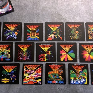 May include: A set of 18 square coasters featuring colorful retro video game graphics with the word "ODYSSEY" printed on each coaster.