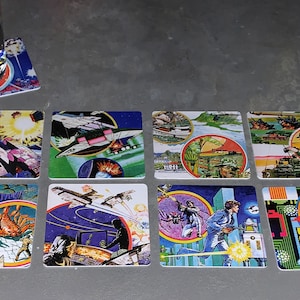 May include: Twelve square coasters with colorful, retro-style illustrations of spaceships, robots, and other futuristic imagery. The coasters are made of a durable material and are perfect for protecting surfaces from spills and scratches.