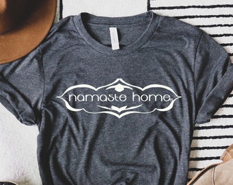 May include: A dark grey t-shirt with a white graphic that says "namaste home" in a decorative font.