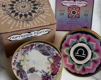 May include: A gold candle tin with a white candle and pink and purple dried flowers and crystals. The lid of the tin has a pink and green mandala design with the astrological symbol for Libra in the center. The text on the lid reads "namaste home" and "libra".