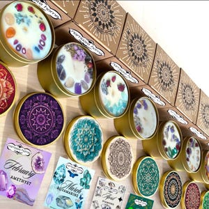 May include: A collection of gold-colored tin candles with various designs and embedded crystals. The candles are arranged with decorative mandala-patterned lids and boxes. The image also includes cards with gemstone names and illustrations.