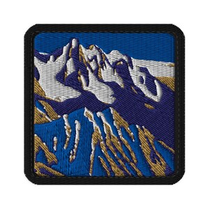 May include: Embroidered patch depicting a mountain range. The design features a mountain landscape with white and gold peaks, set against a blue sky and terrain. The patch has a black border.