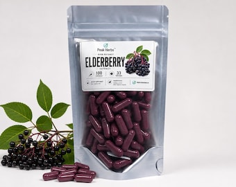 May include: A silver stand-up pouch filled with dark purple capsules, labeled Peak Herbs High Potency Elderberry Extract, 100 capsules, 33 servings. A sprig of fresh elderberries with green leaves sits to the left of the pouch on a white surface.