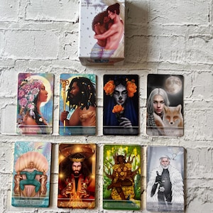 Puede incluir: Un juego de cartas del tarot y un juego de gu&iacute;as con ilustraciones coloridas. La caja muestra a una pareja abraz&aacute;ndose. Se muestran varias cartas del tarot, incluyendo la Emperatriz, el Emperador, la Muerte, la Luna, el Rey de Copas, el Rey de Bastos, el Rey de Oros y el Rey de Espadas.