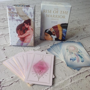 Puede incluir: Se muestran dos mazos de cartas del tarot y una extensi&oacute;n de cartas. Un mazo se titula "The Warrior of Love Tarot" y el otro "The Rise of the Warrior Oracle". Las cartas presentan ilustraciones de figuras y dise&ntilde;os geom&eacute;tricos, con una paleta de colores suaves.