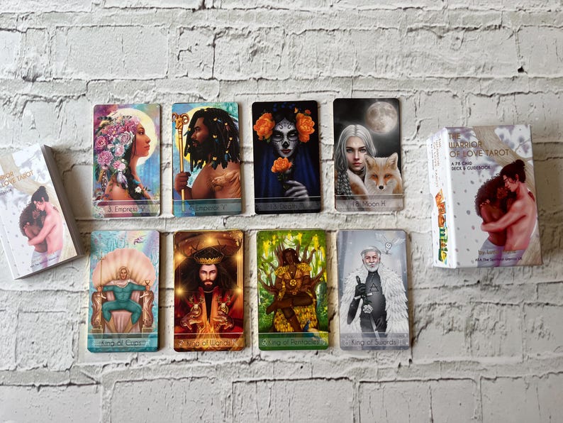 Puede incluir: Un mazo de cartas del tarot y varias cartas individuales se muestran sobre un fondo de ladrillos blancos. Las cartas presentan ilustraciones coloridas de figuras, incluyendo una emperatriz, un emperador y un rey. La caja del mazo muestra dos figuras abraz&aacute;ndose.