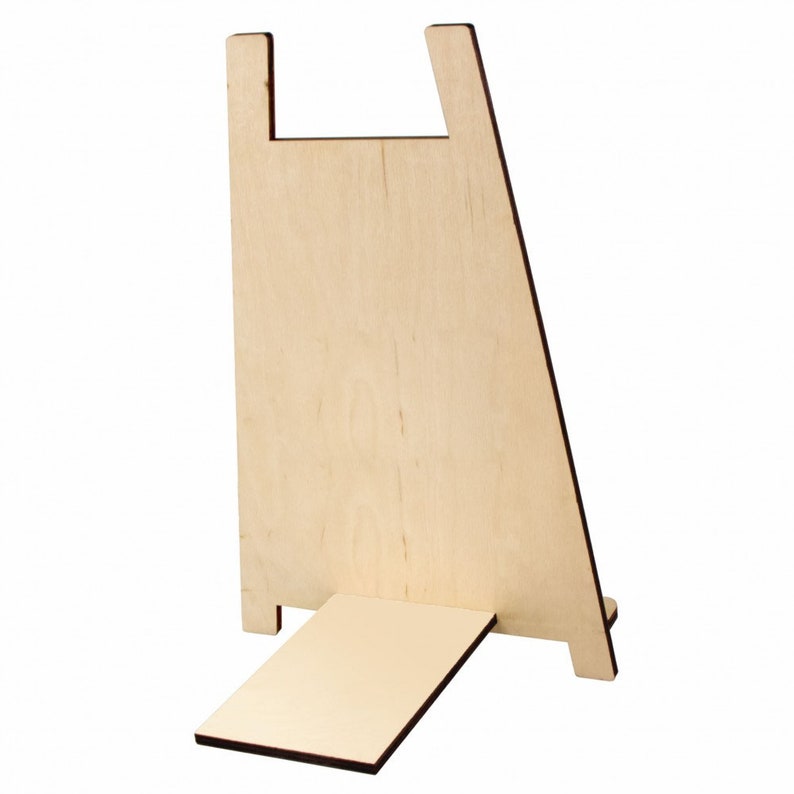 May include: A light-coloured wooden easel with a rectangular base and a back support featuring a notch at the top. The easel is designed to hold a small sign or artwork. The wood has a natural grain.