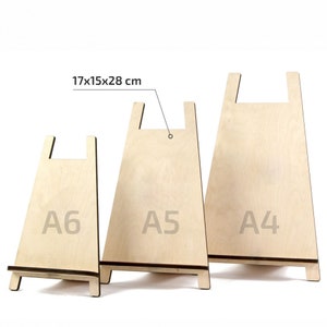 May include: Three wooden display stands in different sizes, labelled A6, A5, and A4. The stands are made of light-coloured wood and have a simple design. The largest stand measures 17x15x28 cm.
