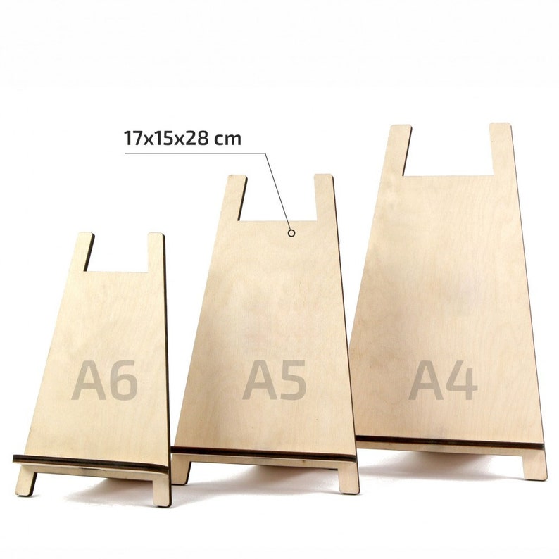 May include: Three wooden display stands in different sizes, labelled A6, A5, and A4. The stands are made of light-coloured wood and have a simple design. The largest stand measures 17x15x28 cm.