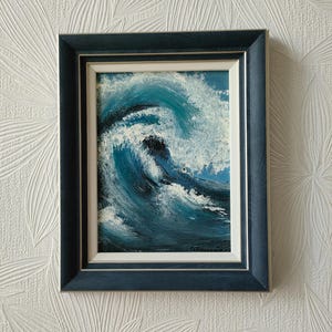 May include: A framed painting of a blue ocean wave crashing with white foam. The painting is in a dark blue frame with a white mat.